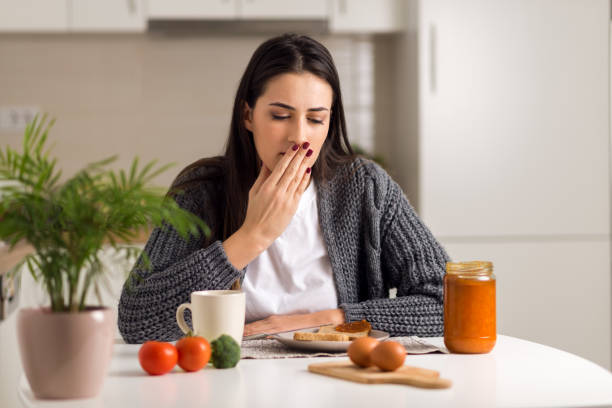Woman yawning at a kitchen table with food and a plant nearby.