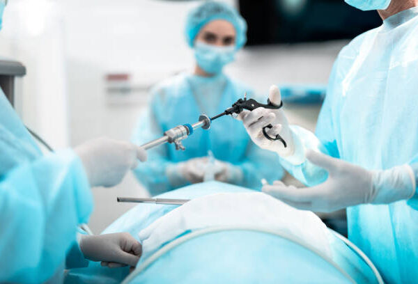 Close up of male and female hands holding laparoscopic grasper with trocar. Female medical worker holding oxygen mask on patient face on blurred background