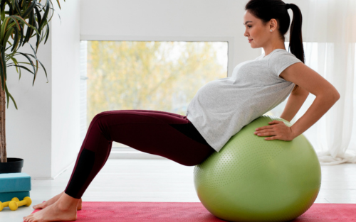 Pregnant woman practicing prenatal exercises with a fitness ball in a bright room.