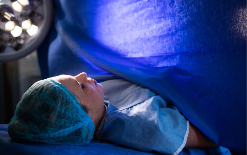 A woman undergoing surgery under blue surgical drapes in a healthcare setting.