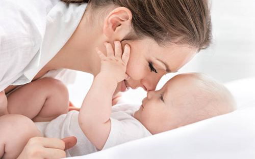 Mother bonding with baby in gentle and loving embrace on white bed.