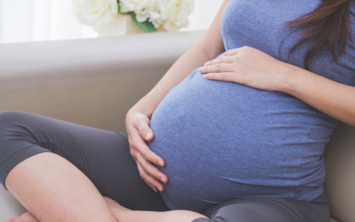 Pregnant woman sitting comfortably on a couch touching her belly
