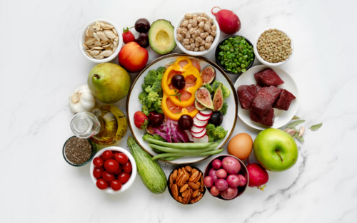 A variety of fresh fruits nuts vegetables and meats arranged artfully on a table.